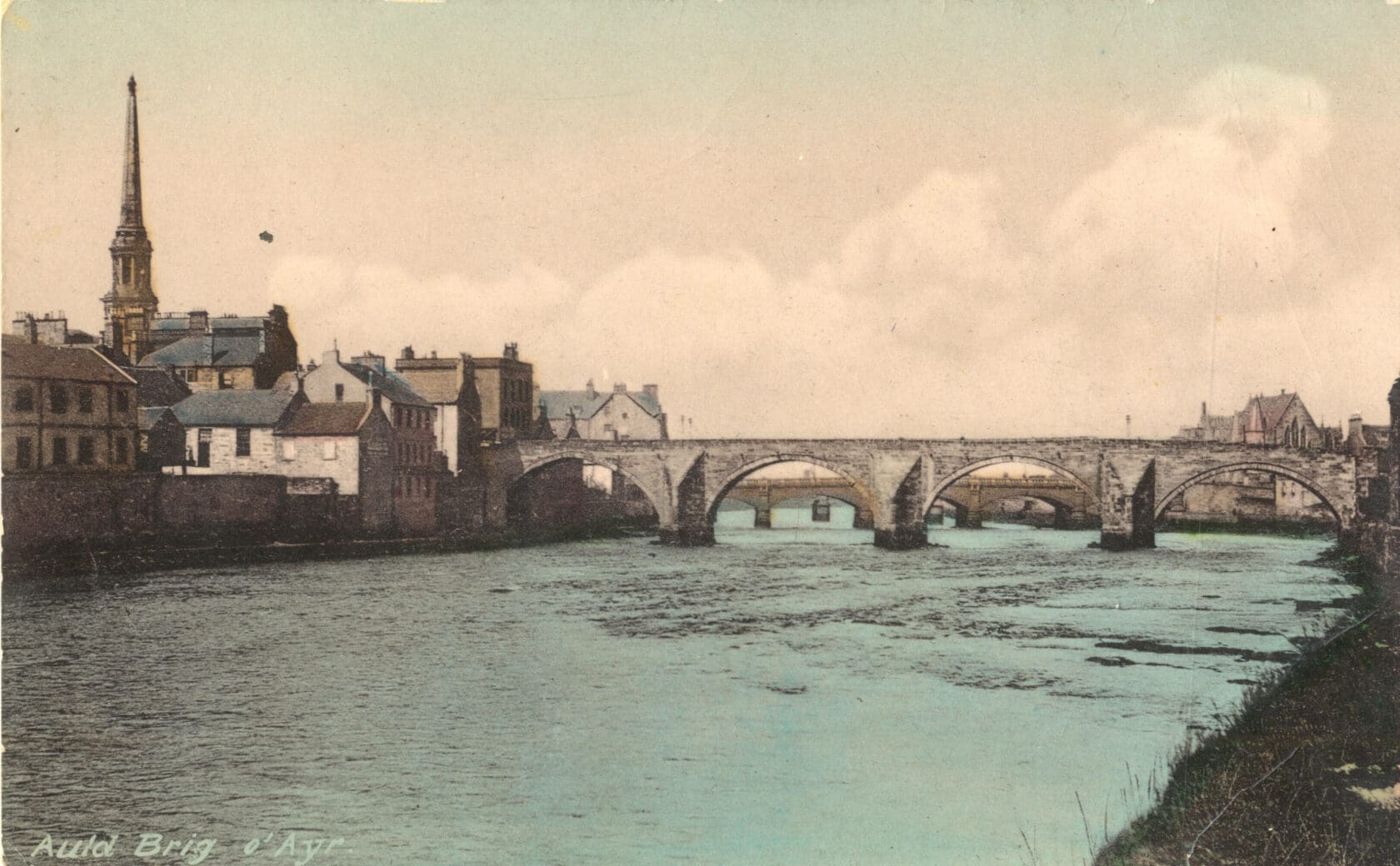 A colorized photograph of a wide river spanned by several multi-arched stone bridges. Buildings flank both banks. On the left and nearer side, one tall spire rises above all the surrounding structures.
