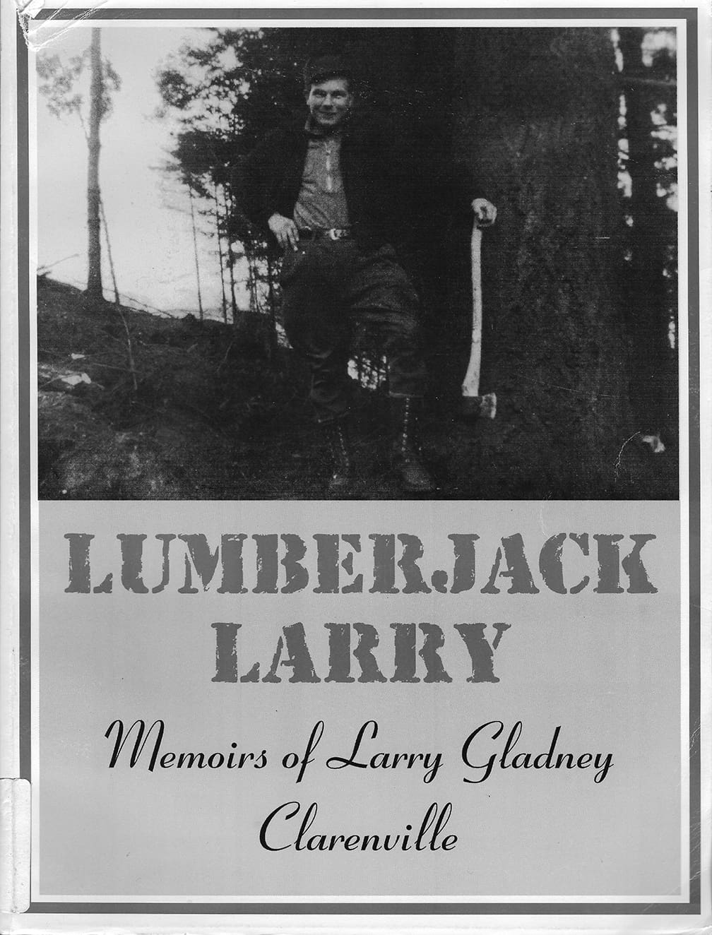 The cover of a book titled Lumberjack Larry. Filling its top half is a photograph of a smiling man in work clothes standing on a half-cut hillside. His right hand is on hip and his left rests on the upright end of his axe handle.
