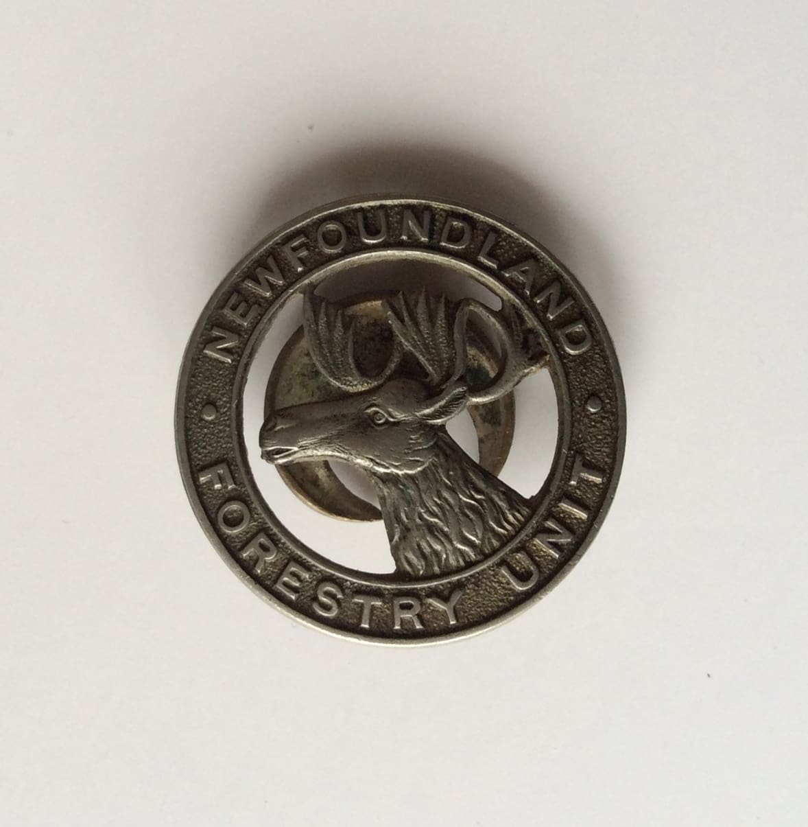 A documentary photograph of a metal pin. The Unit’s name is imprinted on an exterior circle. Inside it are the head and antlers of a caribou.