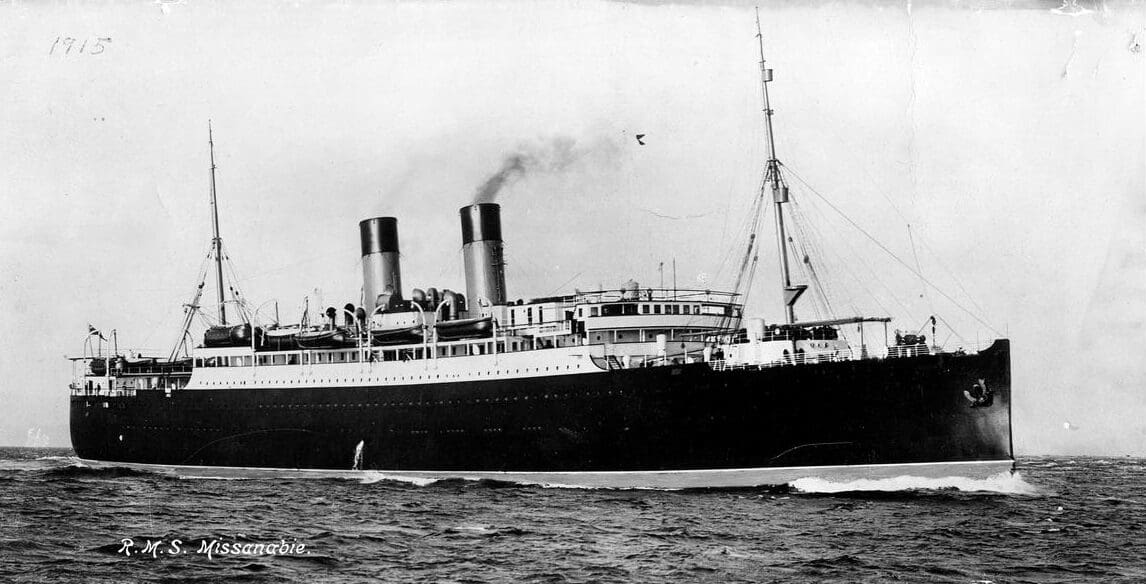 A black and white photograph of the starboard side of a dark-hulled steamship with two funnels. Its waterline is visible and a bow wave streams back from its stem as it steams over open ocean from left to right.