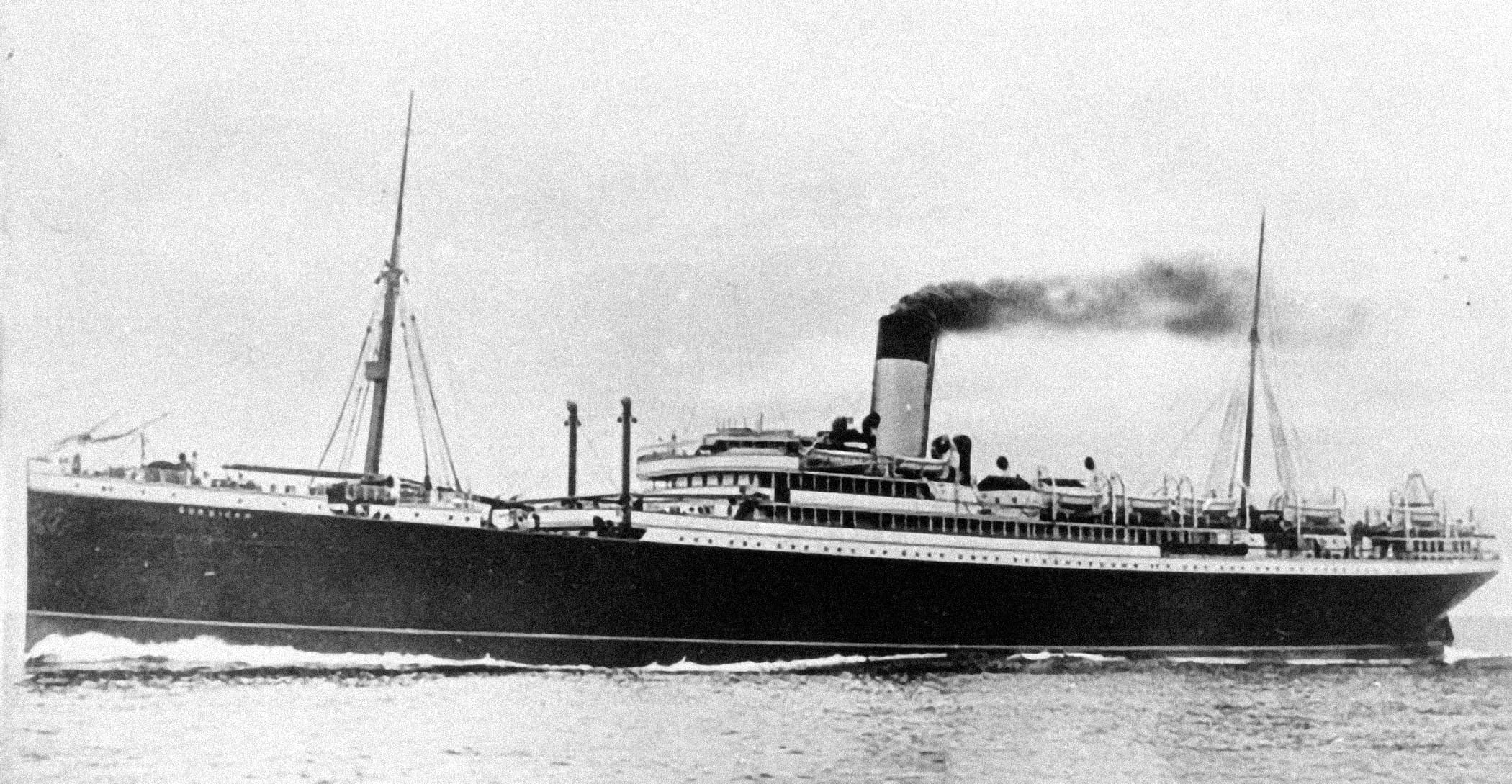 A side-on, black and white image of a dark-hulled ship moving at speed over smooth waters, travelling from right to left. It has two masts and, amidships, a tall funnel belching dark smoke.