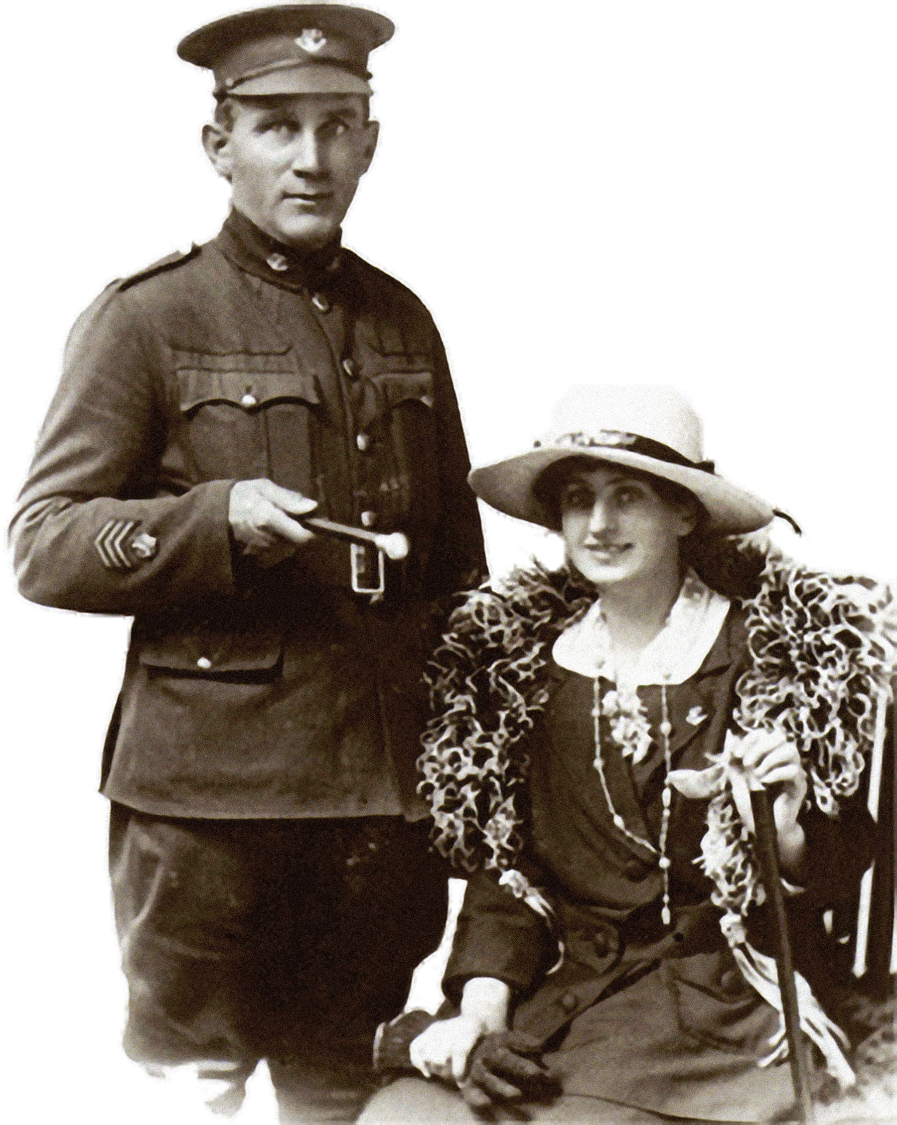 A sepia photograph of a man in uniform, a baton held under his arm, standing to the left of a seated woman in a wide-brimmed white hat. She wears dark clothes, clasps her gloves in her right hand, and smiles at the camera. A stole rests around her shoulders.