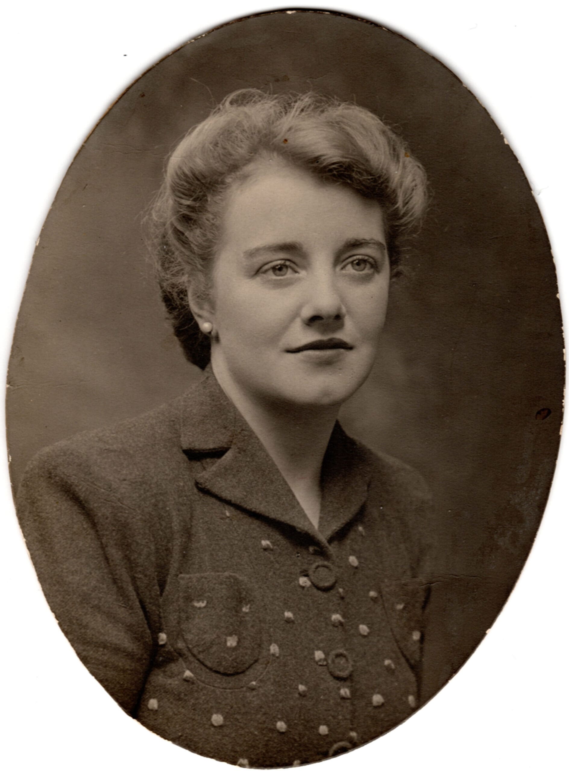 A sepia, oval, head-and-shoulders studio portrait of a young woman. Her dark hair is swept back and pinned up; one pearl stud earring is visible. She has large light-coloured eyes, a clear complexion and a slight dimple in her chin.