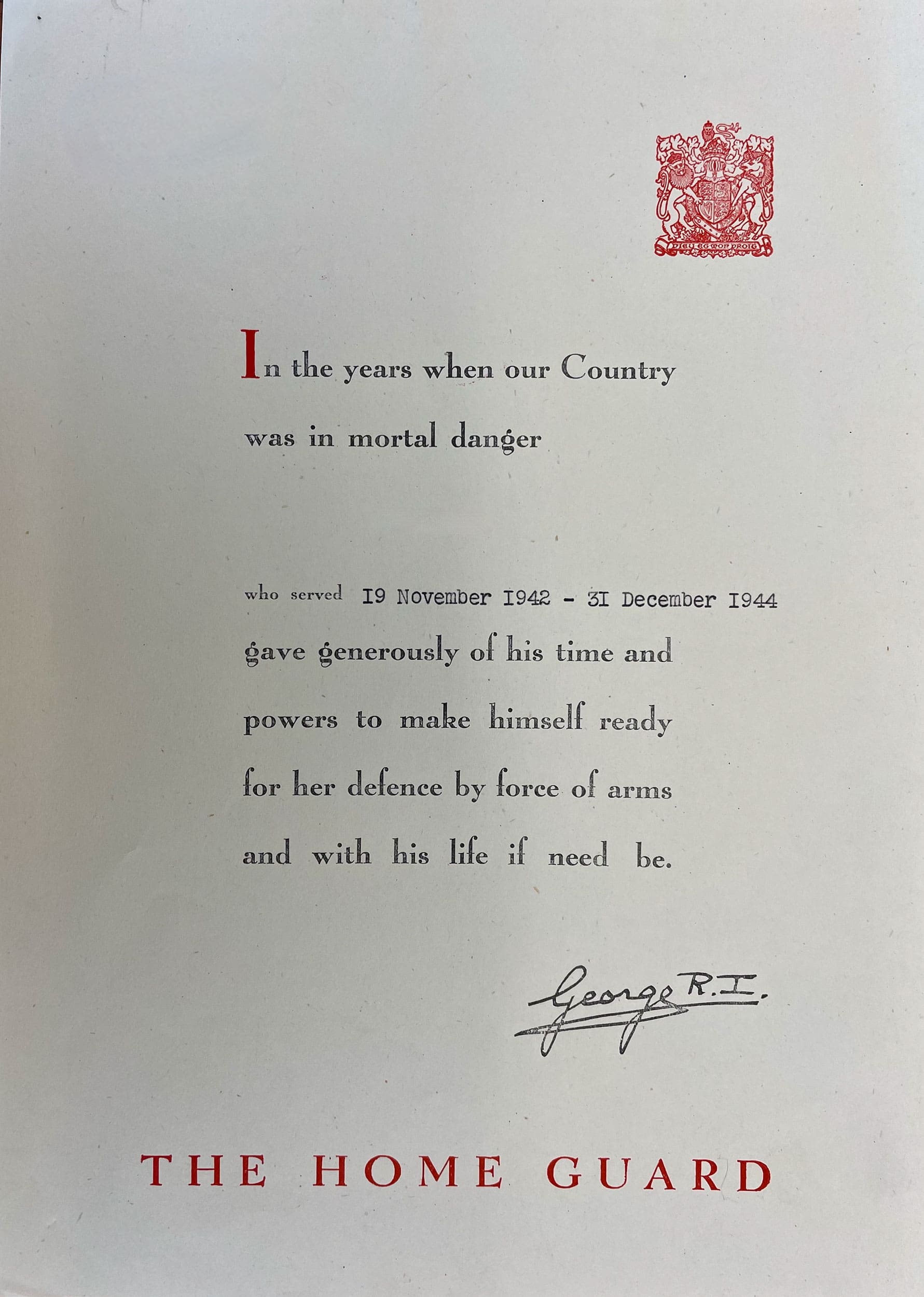 A short text noting dates of volunteer service is centred on a white page. The Royal Coat of Arms, printed in red, is in the upper right-hand corner. The text reads: In the years when our Country was in mortal danger . . . [blank space left for name insertion] . . . who served 19 November 1942 – 31 December 1944 gave generously of is time and powers to make himself ready for her defence by force of arms and with his life if need be. George R.I. THE HOME GUARD